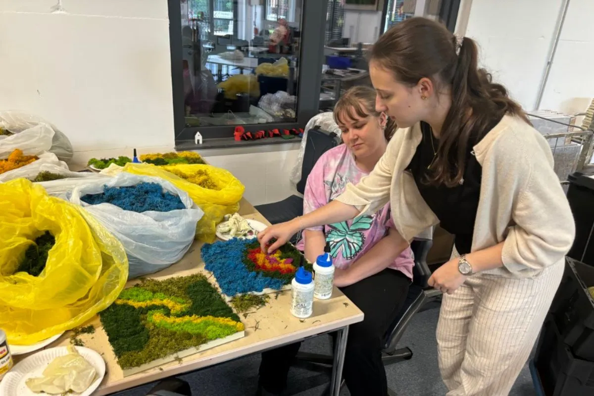 Zwei Personen arbeiten gemeinsam an einem bunten Moosbild.