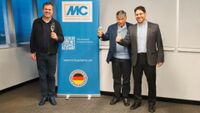 Drei Personen stehen vor einem blauen Schild und stoßen auf die Gründung einer neuen Gesellschaft der MC-Bauchemie an.