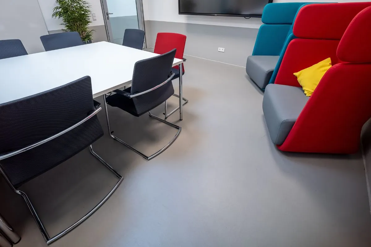 Blick in einen Raum mit einem glatten Boden, Tisch, Stühlen und weiteren Sitzgelegenheiten