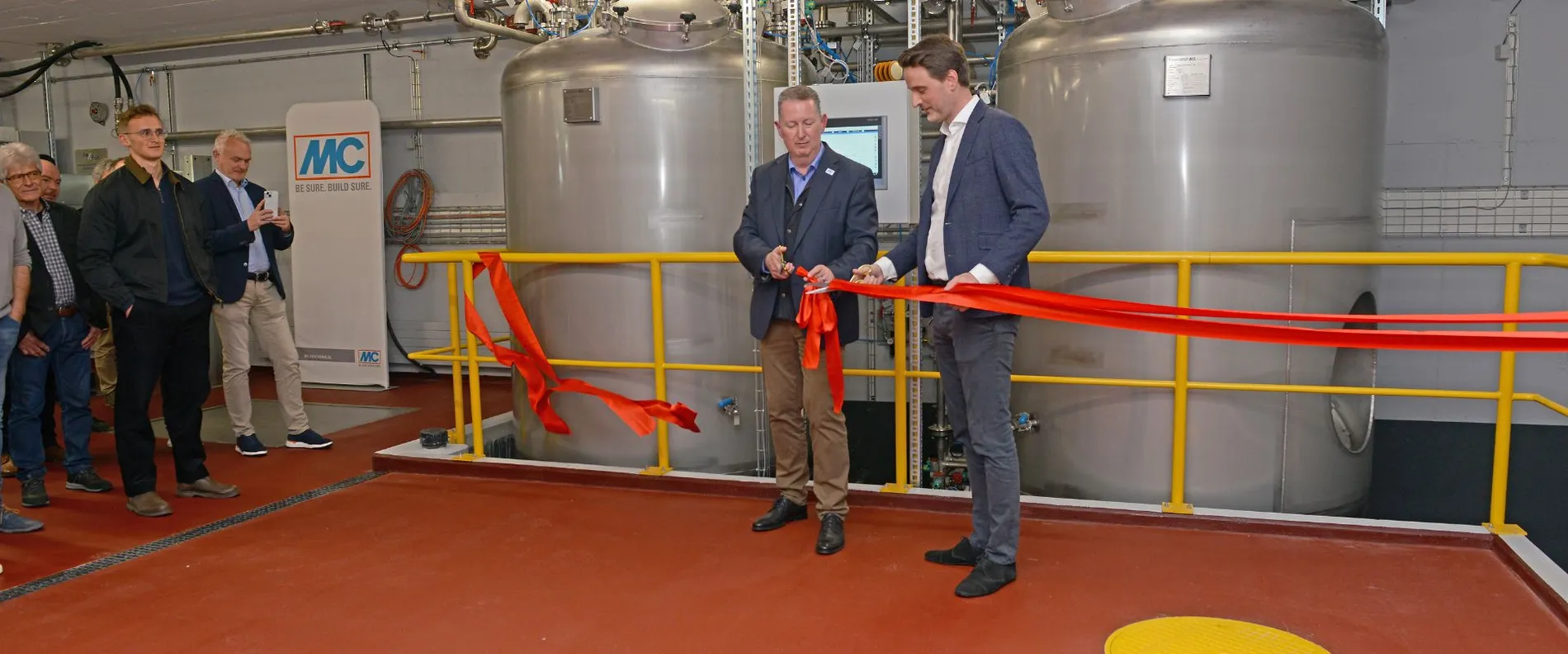 Timur Rönnert und Nicolaus Müller schneiden ein rotes Band vor der neuen Produktionsanlage durch.